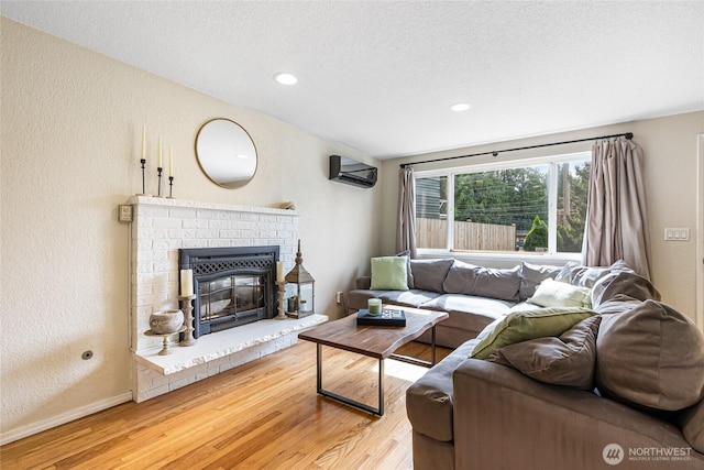 26600 Weaver Ave NW, Poulsbo, WA 98370 - living room featuring light wood finished floors, a textured wall, a textured ceiling, a fireplace, and a wall mounted air conditioner
