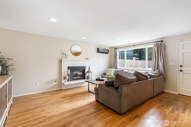 26600 Weaver Ave NW, Poulsbo, WA 98370 - living area featuring a wall unit AC, light wood-type flooring, a textured ceiling, a brick fireplace, and recessed lighting