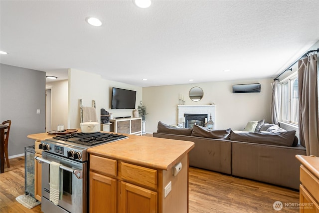 26600 Weaver Ave NW, Poulsbo, WA 98370 - kitchen featuring stainless steel range with gas cooktop, open floor plan, light wood-style flooring, a wall mounted air conditioner, and a fireplace