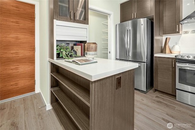 1760 NW 56th St Unit 608, Seattle, WA 98107 - kitchen with stainless steel appliances, open shelves, wall chimney exhaust hood, light countertops, and light wood-style flooring