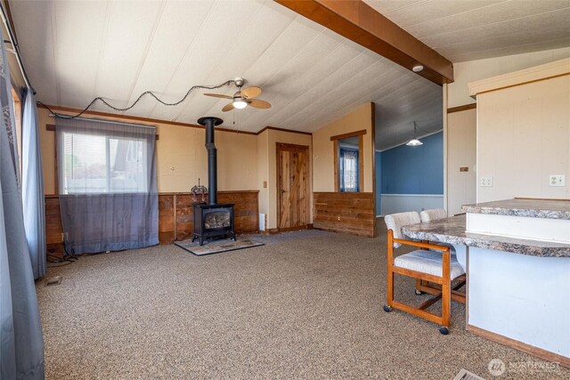 7515 Sunset Dr, Blaine, WA 98230 - carpeted living room with a wood stove, a ceiling fan, lofted ceiling, wooden walls, and a wainscoted wall