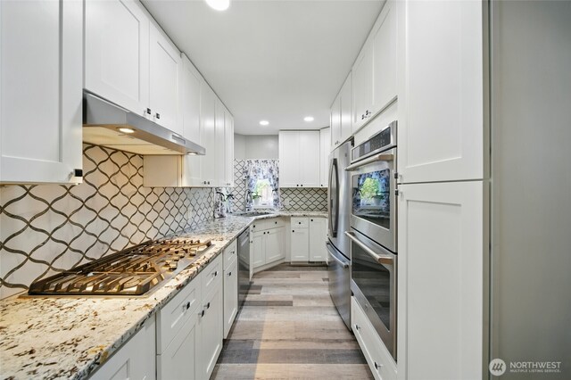 513 SE Highland Park Dr, College Place, WA 99324 - kitchen featuring under cabinet range hood, appliances with stainless steel finishes, light wood-type flooring, white cabinets, and decorative backsplash