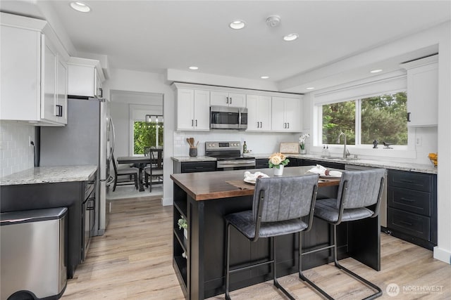 9906 328th St E, Graham, WA 98338 - kitchen featuring stainless steel appliances, white cabinets, a sink, a breakfast bar area, and backsplash