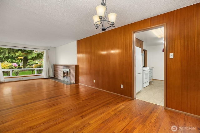 10210 NE 23rd St, Bellevue, WA 98004 - unfurnished living room with a chandelier, light wood-type flooring, wood walls, a fireplace, and a textured ceiling