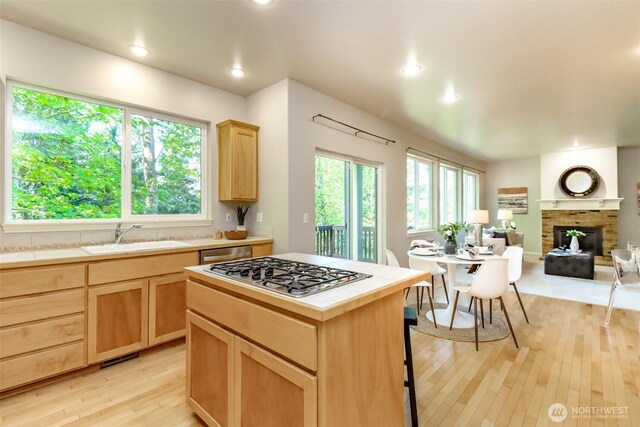 1913 NE 32nd St, Renton, WA 98056 - kitchen with tile counters, appliances with stainless steel finishes, light brown cabinetry, a brick fireplace, and light wood-style flooring