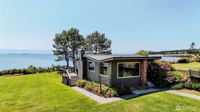62 Wildwood Ln, Lopez Island, WA 98261 - view of front of house with a chimney, a front yard, a deck with water view, and a metal roof