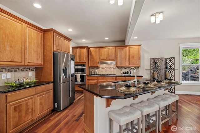 7320 111th Pl SE, Newcastle, WA 98056 - kitchen featuring appliances with stainless steel finishes, dark wood finished floors, dark countertops, under cabinet range hood, and a kitchen breakfast bar