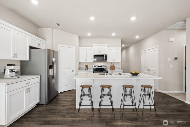 7402 281st Pl NW Unit 75, Stanwood, WA 98292 - kitchen with stainless steel appliances, white cabinetry, a breakfast bar, a kitchen island with sink, and dark wood-style floors