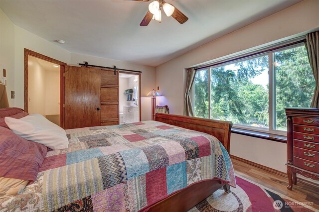 22305 Apollo Dr NE, Poulsbo, WA 98370 - bedroom featuring wood finished floors, a barn door, baseboards, connected bathroom, and ceiling fan