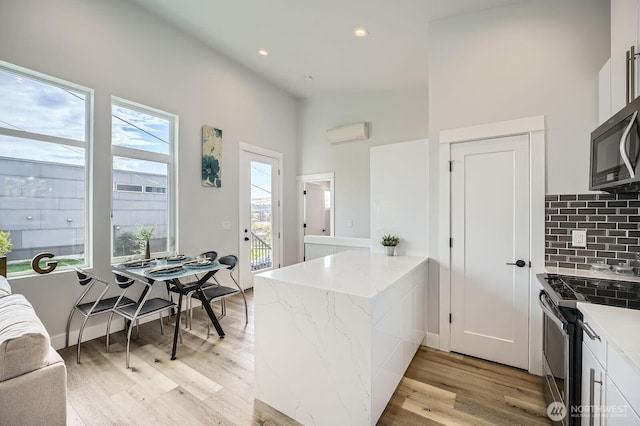 1808 S Raymond St, Seattle, WA 98108 - kitchen featuring appliances with stainless steel finishes, a peninsula, decorative backsplash, light wood-type flooring, and light stone countertops