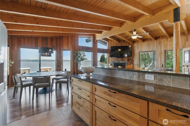 6570 E Grapeview Loop Rd, Allyn, WA 98524 - kitchen with wood walls, a lit fireplace, dark stone countertops, ceiling fan, and open floor plan