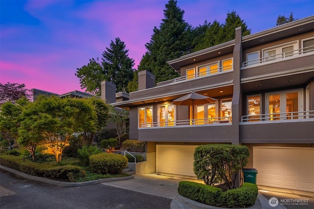 740 1st St S, Kirkland, WA 98033 - back of house at dusk featuring a balcony, an attached garage, stucco siding, and a chimney