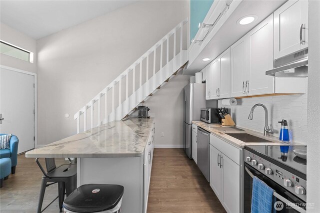 8903 Crescent Bar Rd Unit 158, Quincy, WA 98848 - kitchen featuring stainless steel appliances, under cabinet range hood, a kitchen breakfast bar, white cabinets, and wood finished floors