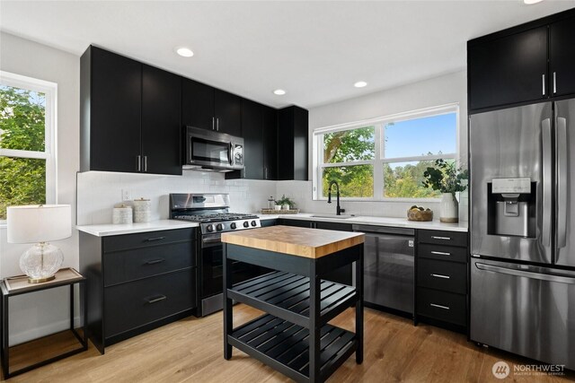 6014 40th Ave NE Unit B, Seattle, WA 98115 - kitchen featuring appliances with stainless steel finishes, dark cabinetry, decorative backsplash, light wood-style flooring, and recessed lighting