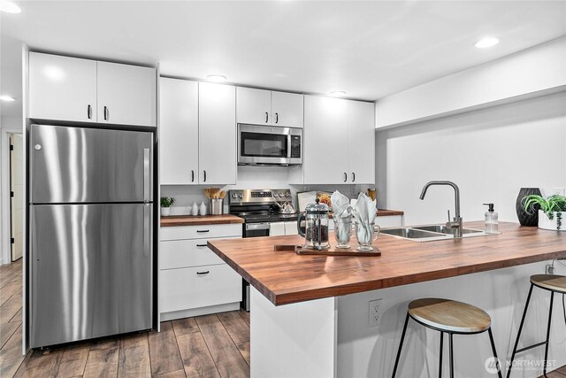 8068 Niska Rd, Blaine, WA 98230 - kitchen with butcher block counters, appliances with stainless steel finishes, a kitchen breakfast bar, dark wood-style floors, and white cabinetry