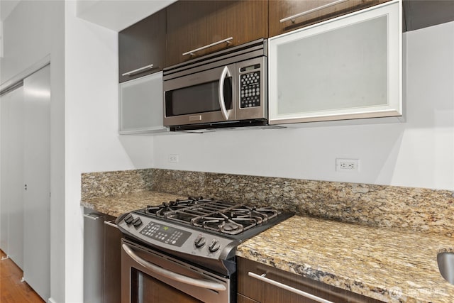 2911 2nd Ave Unit 522, Seattle, WA 98121 - kitchen featuring stainless steel appliances, dark brown cabinets, light stone counters, and wood finished floors