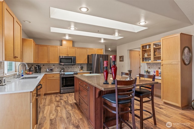 2951 Premiere Pl, Longview, WA 98632 - kitchen with appliances with stainless steel finishes, a sink, a skylight, a kitchen breakfast bar, and light wood-style flooring