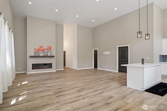 10642 Merry Canyon Rd, Leavenworth, WA 98820 - unfurnished living room featuring a high ceiling, a glass covered fireplace, light wood finished floors, baseboards, and recessed lighting