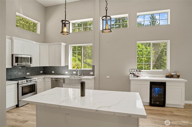 10642 Merry Canyon Rd, Leavenworth, WA 98820 - kitchen featuring appliances with stainless steel finishes, a high ceiling, beverage cooler, light wood-type flooring, and white cabinetry
