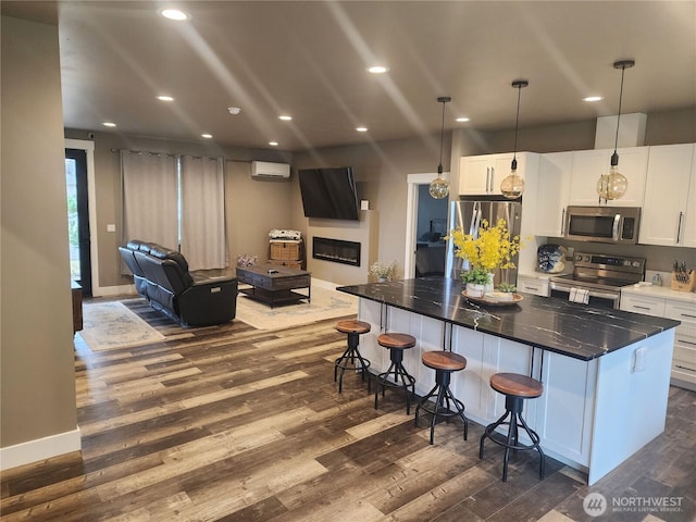 613 Aster Ct SE, Ocean Shores, WA 98569 - kitchen with stainless steel appliances, dark wood-type flooring, a wall unit AC, a breakfast bar area, and open floor plan