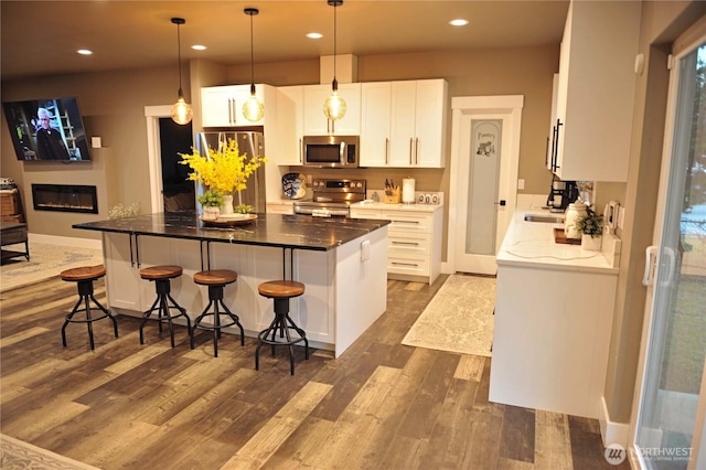 613 Aster Ct SE, Ocean Shores, WA 98569 - kitchen with stainless steel appliances, dark wood-type flooring, white cabinetry, a kitchen island, and a breakfast bar