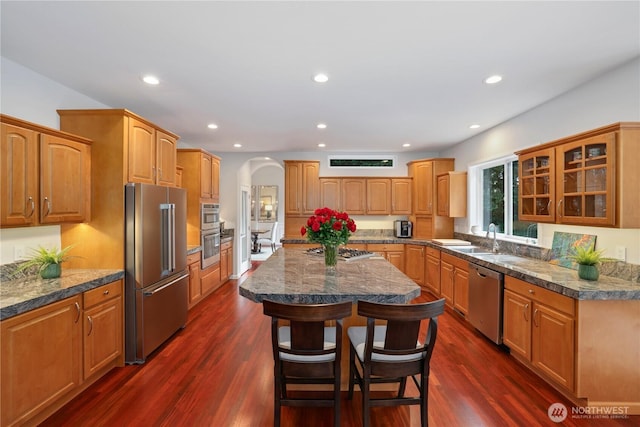 7531 Hawkstone Ave SW, Port Orchard, WA 98367 - kitchen featuring stainless steel appliances, arched walkways, glass insert cabinets, a kitchen island, and a breakfast bar