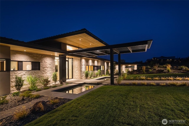 335 Brickwood Dr, Walla Walla, WA 99362 - back of house at night featuring stone siding, a lawn, and an outdoor pool