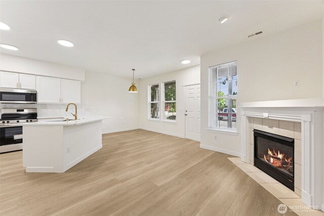 717 115th St E, Tacoma, WA 98445 - kitchen with appliances with stainless steel finishes, light wood-type flooring, light countertops, white cabinets, and a tile fireplace