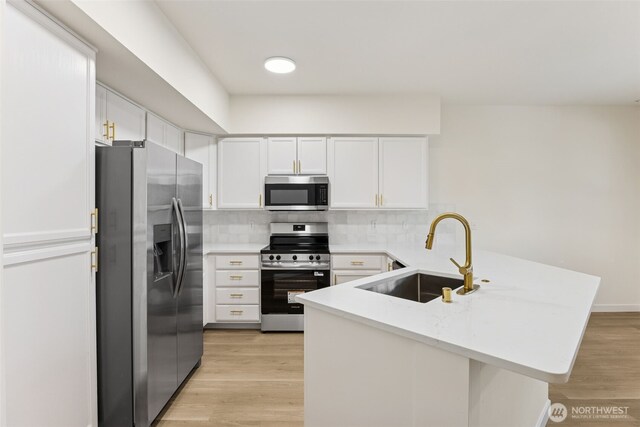 717 115th St E, Tacoma, WA 98445 - kitchen featuring appliances with stainless steel finishes, a peninsula, backsplash, white cabinets, and light wood finished floors