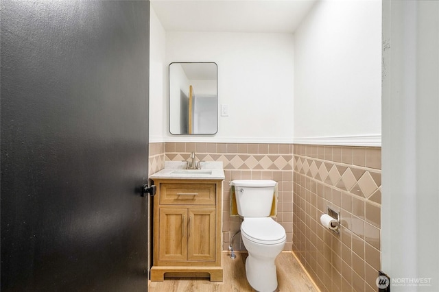 449 NE Cliff Ave, Wilbur, WA 99185 - bathroom featuring toilet, vanity, a wainscoted wall, tile walls, and wood finished floors