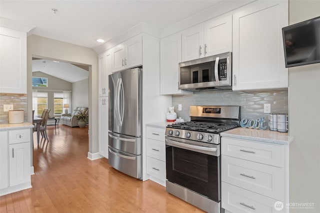 7114 Hazel Pl SE, Auburn, WA 98092 - kitchen featuring appliances with stainless steel finishes, lofted ceiling, light wood finished floors, white cabinetry, and tasteful backsplash