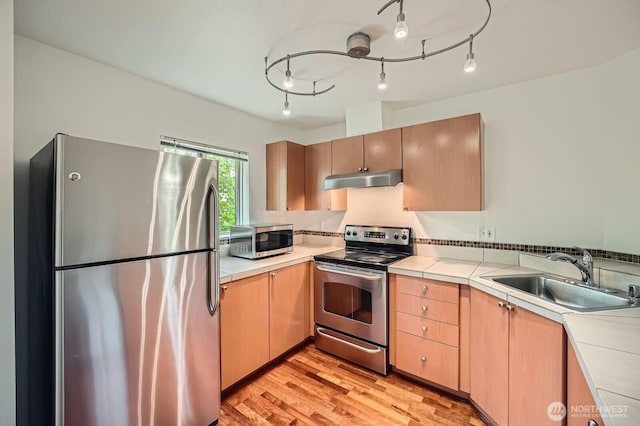 621 5th Ave N Unit 306, Seattle, WA 98109 - kitchen with appliances with stainless steel finishes, a sink, under cabinet range hood, light wood-style flooring, and light brown cabinets