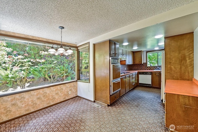 2781 Lake Whatcom Blvd, Bellingham, WA 98229 - kitchen with white dishwasher, a chandelier, brown cabinetry, oven, and under cabinet range hood