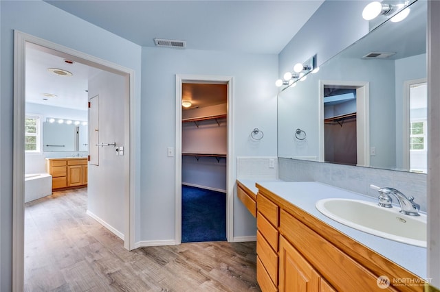 2800 Cliff St, Port Townsend, WA 98368 - bathroom featuring two vanities, wood finished floors, a walk in closet, a garden tub, and plenty of natural light