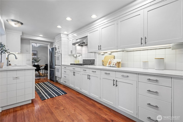 7979 NE 28th St, Medina, WA 98039 - kitchen featuring decorative backsplash, exhaust hood, light countertops, wood finished floors, and white cabinetry