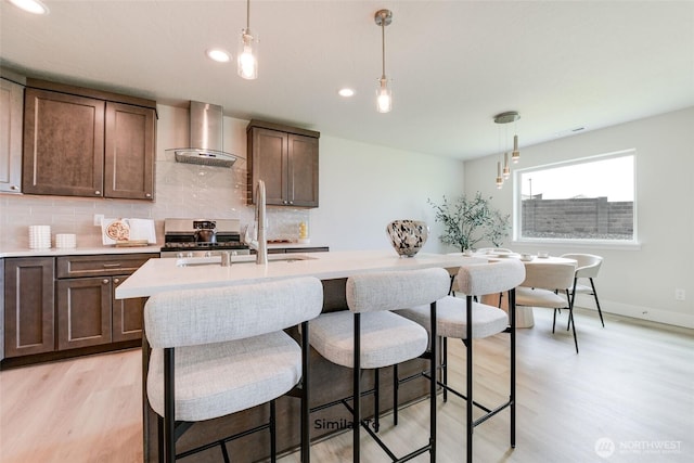 4246 W Sandy Ct, Moses Lake, WA 98837 - kitchen featuring wall chimney exhaust hood, stainless steel stove, light countertops, light wood-style flooring, and backsplash