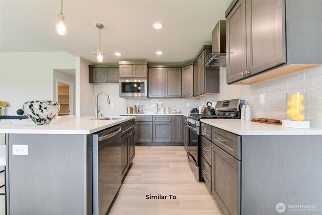 4246 W Sandy Ct, Moses Lake, WA 98837 - kitchen featuring stainless steel appliances, wall chimney exhaust hood, light wood-style floors, decorative backsplash, and an island with sink