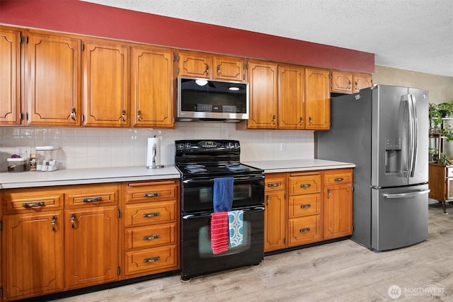209 Old Hill Rd, Aberdeen, WA 98520 - kitchen with stainless steel appliances, brown cabinetry, light countertops, light wood finished floors, and a textured ceiling
