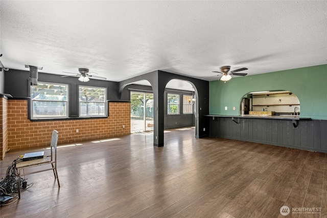 223 Carswell Dr, Moses Lake, WA 98837 - unfurnished living room with a ceiling fan, a textured ceiling, wood finished floors, a wainscoted wall, and arched walkways