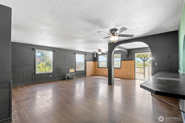 223 Carswell Dr, Moses Lake, WA 98837 - unfurnished living room with ceiling fan, arched walkways, a textured ceiling, wood finished floors, and wainscoting