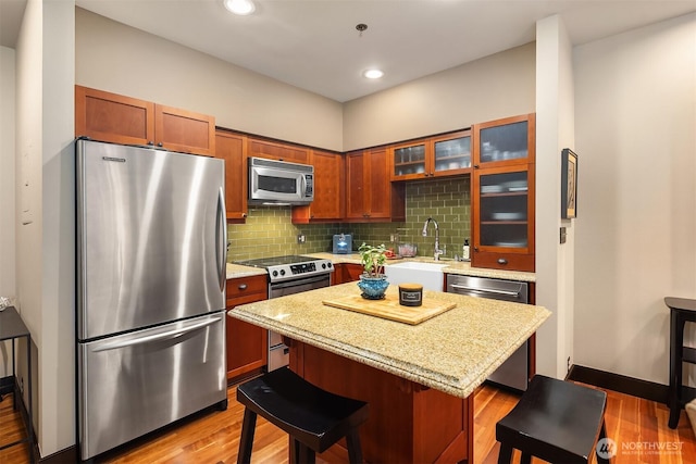 201 Galer St Unit 102, Seattle, WA 98109 - kitchen with appliances with stainless steel finishes, a kitchen breakfast bar, glass insert cabinets, light wood-style flooring, and decorative backsplash