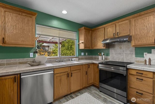 2004 15th Ave SW, Olympia, WA 98502 - kitchen with stainless steel appliances, under cabinet range hood, tile countertops, light wood finished floors, and tasteful backsplash