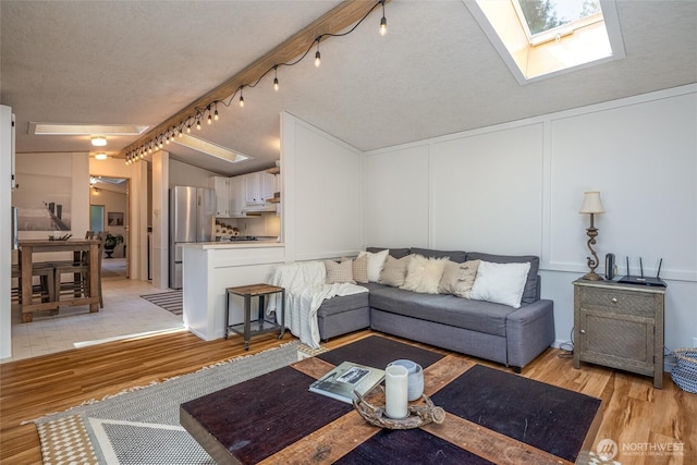316 W Lake Samish Dr Unit 10, Bellingham, WA 98229 - living room featuring a skylight, light wood-type flooring, a decorative wall, vaulted ceiling, and a textured ceiling
