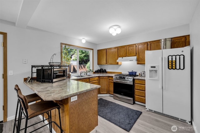 6218 199th Street Ct E, Spanaway, WA 98387 - kitchen with appliances with stainless steel finishes, under cabinet range hood, a peninsula, brown cabinets, and light wood-type flooring