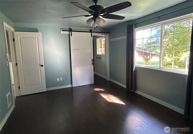 4776 Prairie Ln, Sedro Woolley, WA 98284 - unfurnished bedroom with baseboards, a barn door, dark wood finished floors, and a ceiling fan
