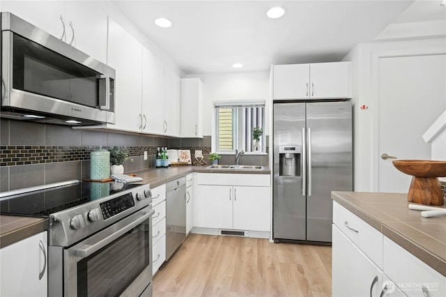 4795 35th Ave S Unit B, Seattle, WA 98118 - kitchen with stainless steel appliances, white cabinets, decorative backsplash, light wood finished floors, and recessed lighting