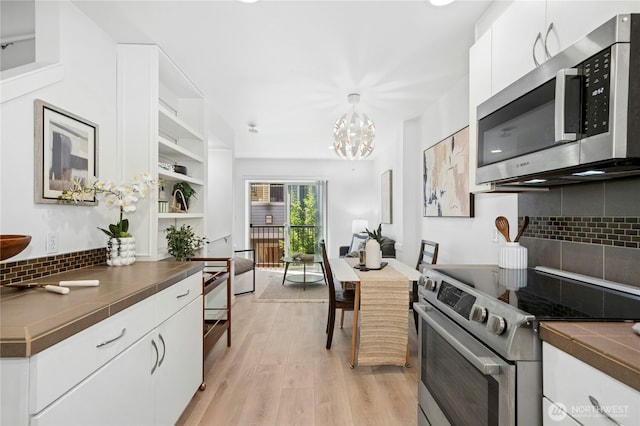 4795 35th Ave S Unit B, Seattle, WA 98118 - kitchen featuring appliances with stainless steel finishes, tasteful backsplash, white cabinets, a chandelier, and light wood-type flooring