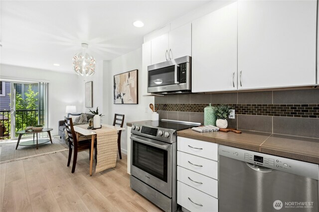 4795 35th Ave S Unit B, Seattle, WA 98118 - kitchen featuring stainless steel appliances, light wood-style flooring, white cabinetry, a chandelier, and tasteful backsplash