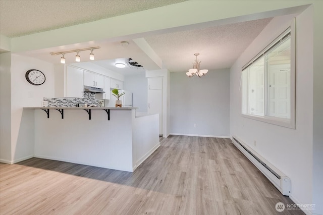 4502 216th St SW Unit 2A, Mountlake Terrace, WA 98043 - kitchen featuring a baseboard heating unit, freestanding refrigerator, under cabinet range hood, a kitchen bar, and light wood finished floors
