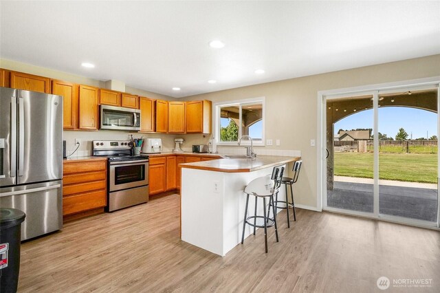 2352 W Covey Dr, Othello, WA 99344 - kitchen featuring appliances with stainless steel finishes, a sink, a peninsula, a kitchen breakfast bar, and light wood-style floors